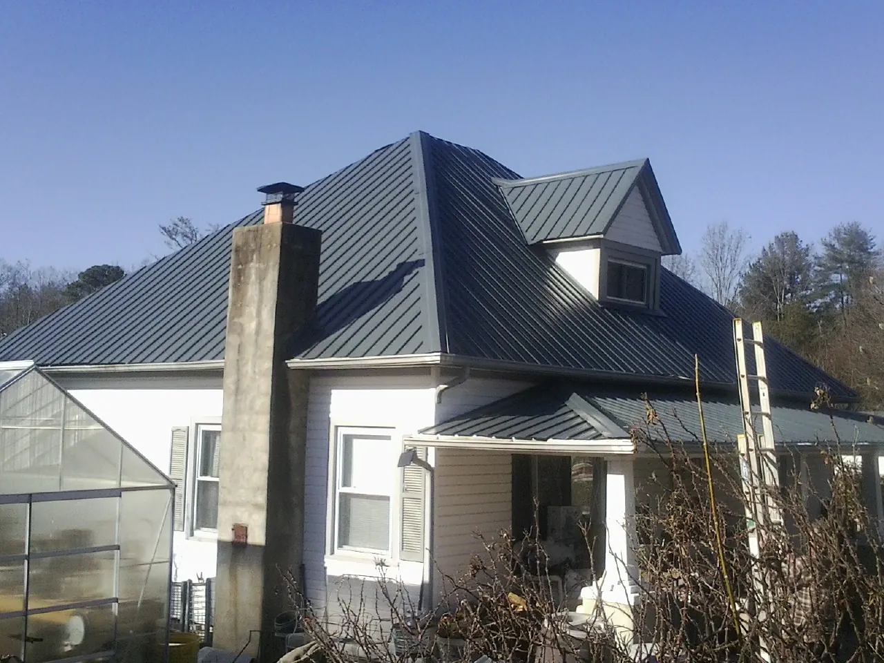 Dark blue standing seam metal roof on a white farmhouse with dormer — Slate & Tile Roof Repair by Roofing Brothers in Florissant