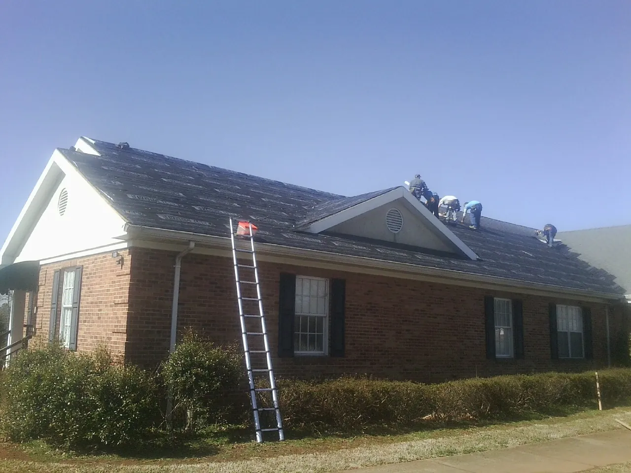 Crew tearing shingles off a brick ranch roof with a ladder set — Metal Roof Repair work by our crew in Florissant
