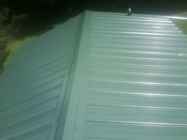 New green metal panels meeting at the ridge of a roof — Flat Roof Repair work by our crew in Florissant