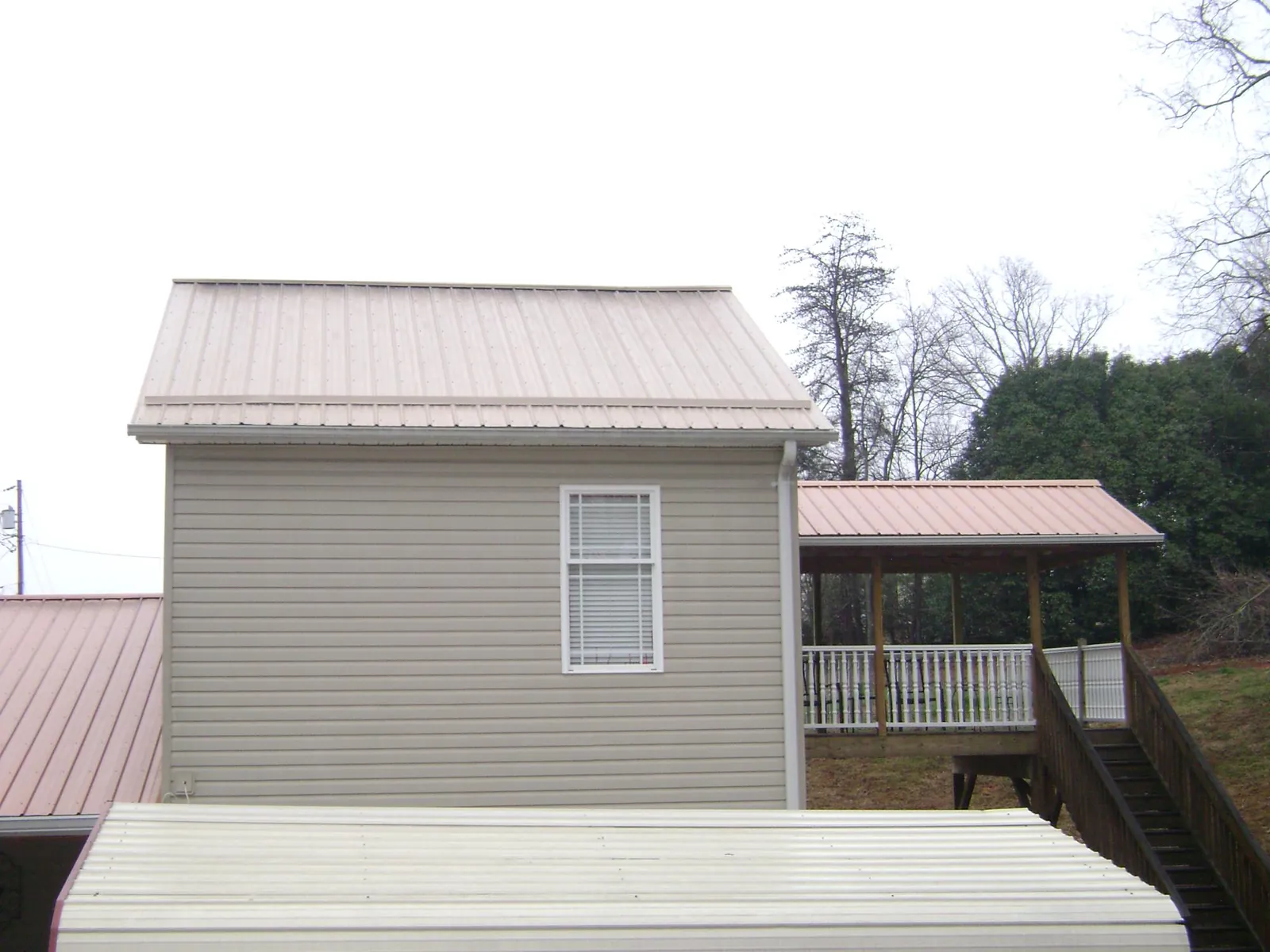 Tan metal roofs on a two story addition and attached porch, from a Roof Replacement job in Florissant